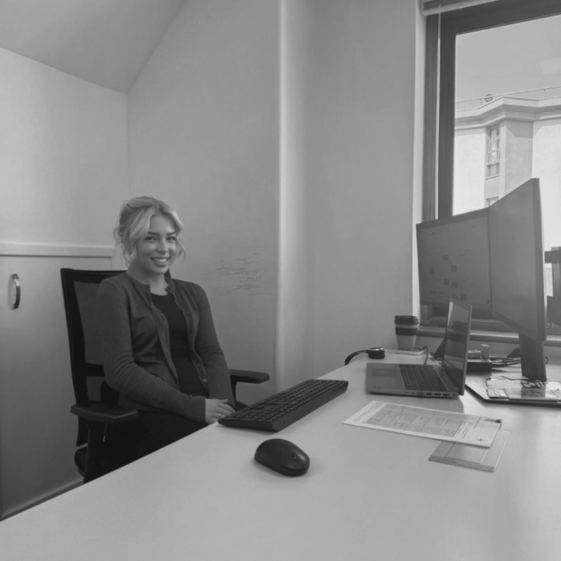 Person working at a desk with two monitors, a laptop, and a coffee cup in an office setting.