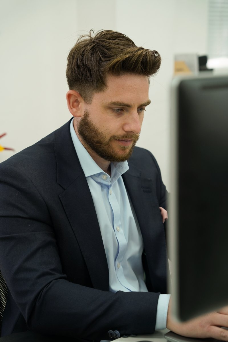 man in navy blue suit with a look of deep concentration whilst he types on a computer keyboard