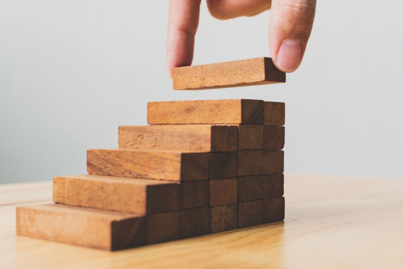 Hand placing a wooden block atop a staircase-like structure made of stacked blocks, symbolising growth, progress, or strategic building.