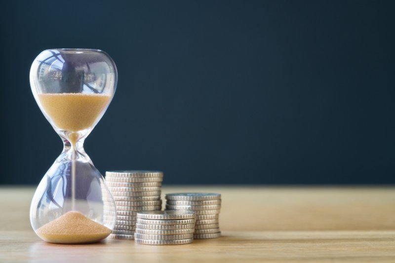 Hourglass with sand flowing beside stacks of coins on a wooden surface, symbolising time, value, and financial efficiency.